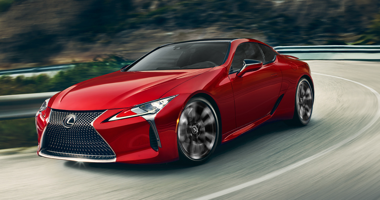 Red Lexus LC 500 driving along a wooded road